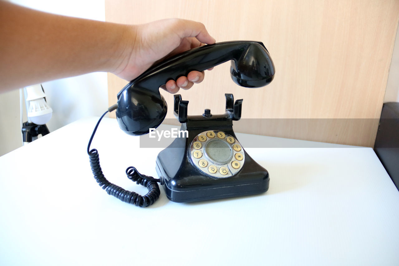 Close-up of hand holding receiver of old landline phone on table