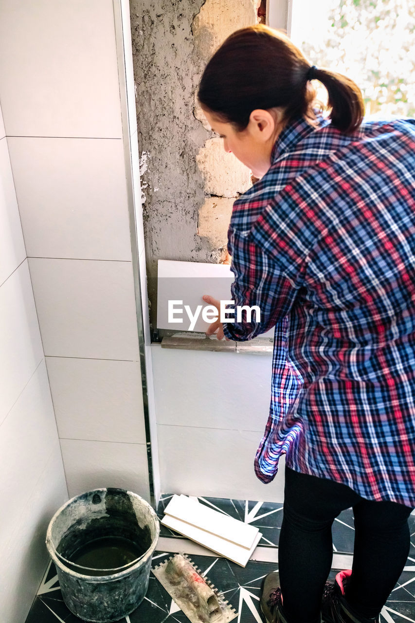 Female bricklayer laying tile on the wall in bathroom renovation