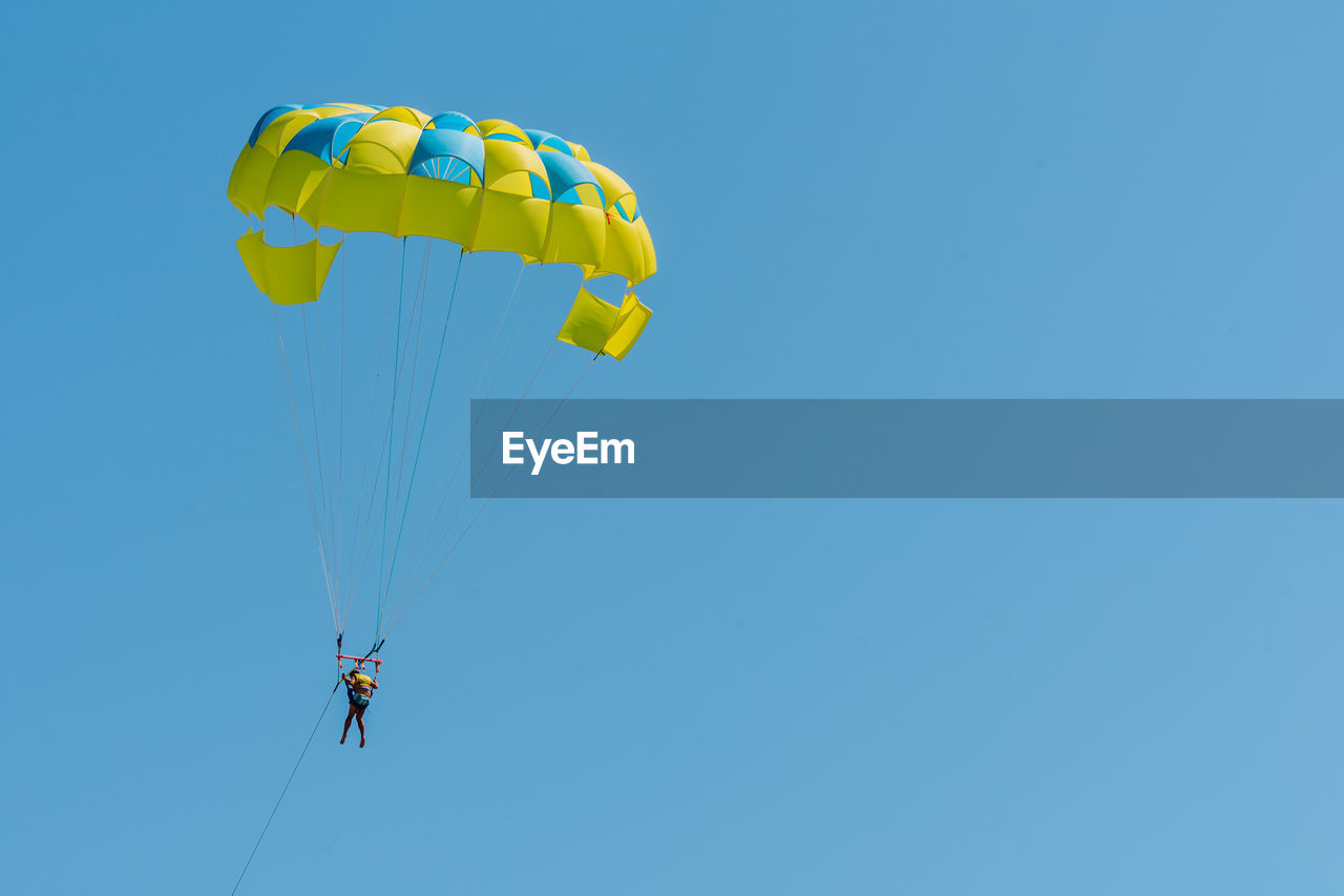 LOW ANGLE VIEW OF PEOPLE FLYING KITE AGAINST CLEAR BLUE SKY