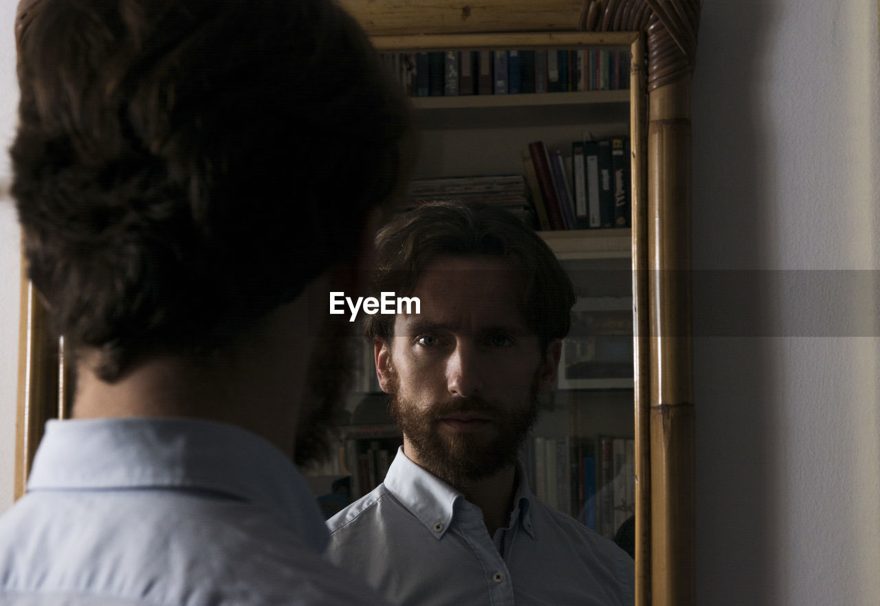 Rear view of confident young man reflecting on mirror at home