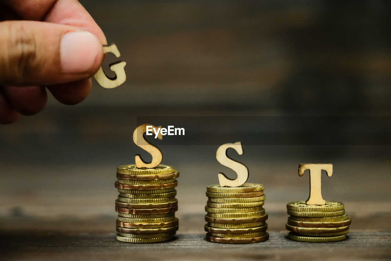 Cropped hand with gst text on stacked coins at table