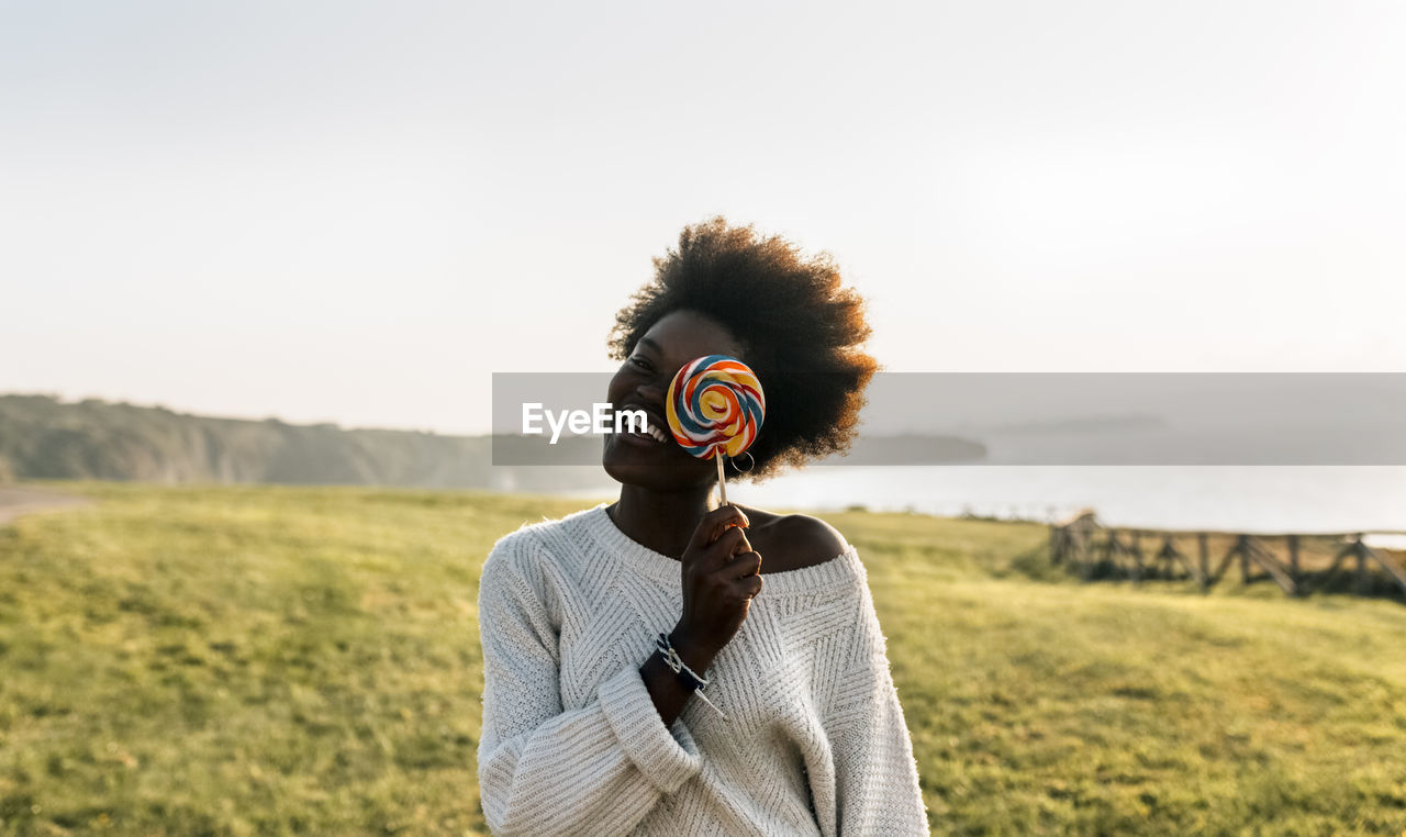 Young woman having covering eye with a lollipop, laughing