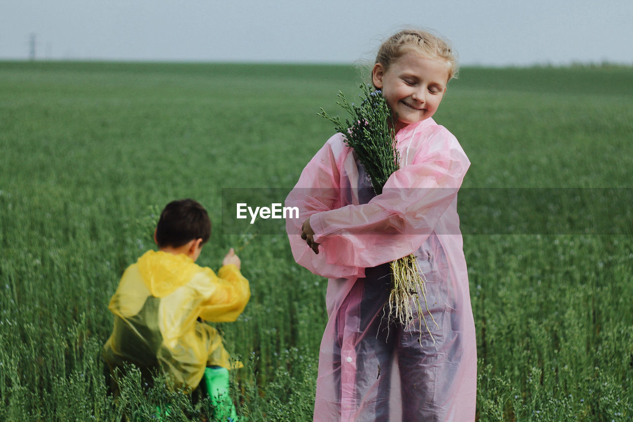 Girl with brother holding plant on field