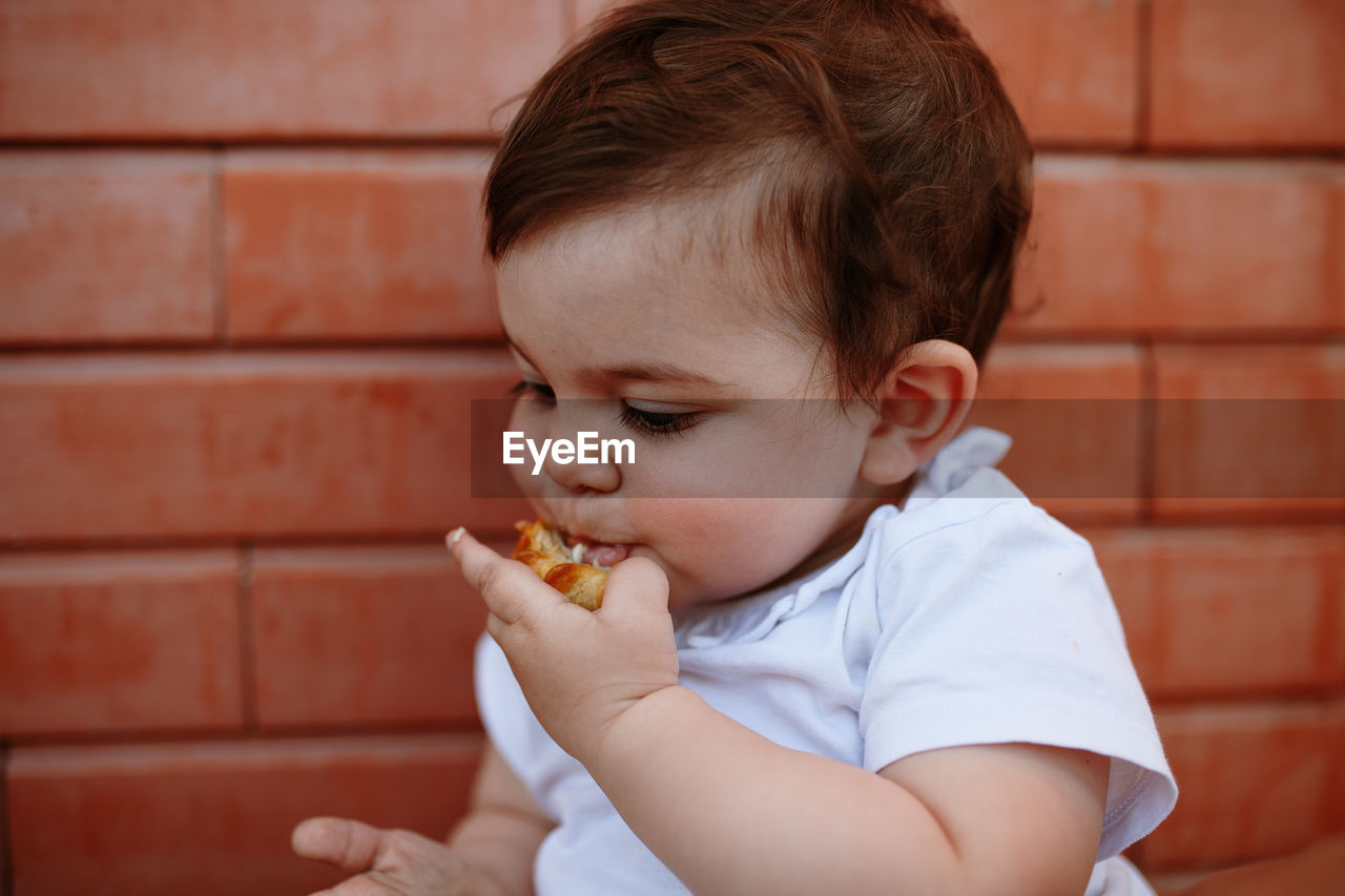 Cute boy eating food against wall