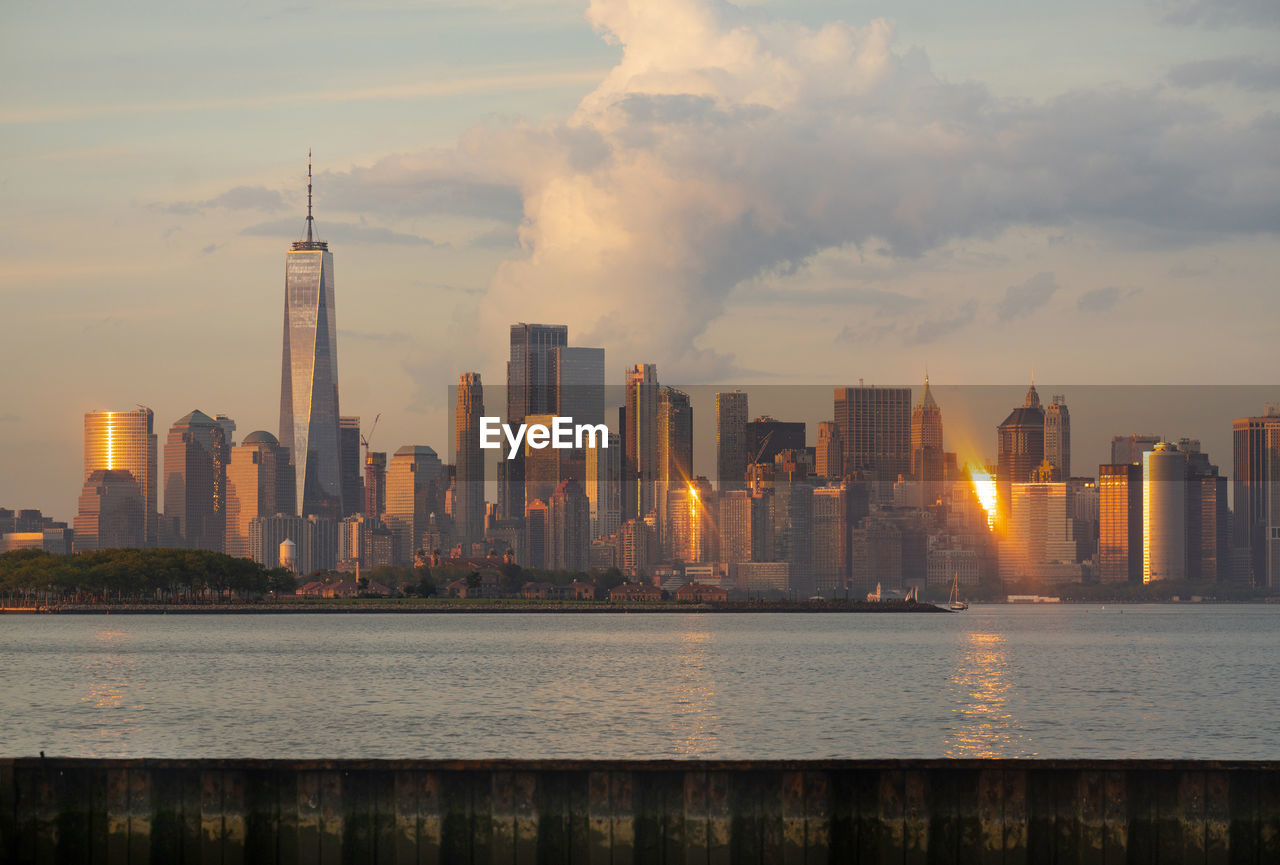 SEA BY MODERN BUILDINGS AGAINST SKY IN CITY DURING SUNSET