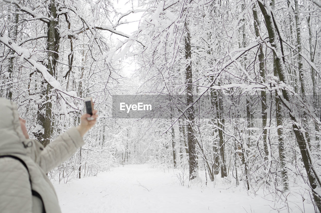 Woman taking selfie on snowy field against bare trees