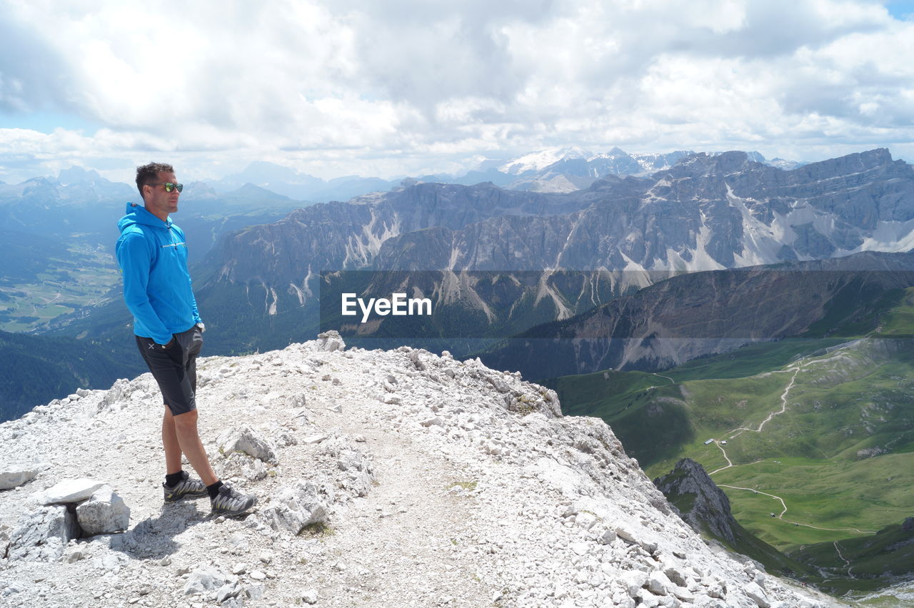 Full length of man standing on peak against rocky mountains and cloudy sky