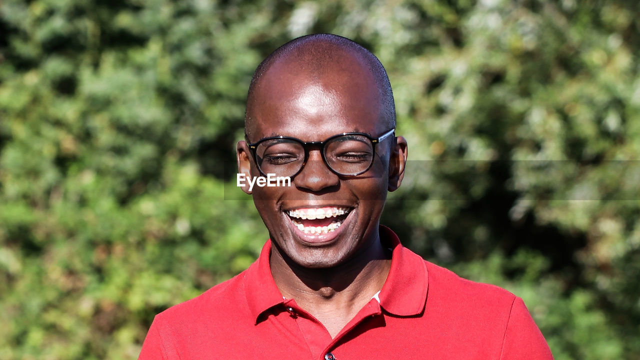 Close-up of young man wearing eyeglasses while laughing against plants