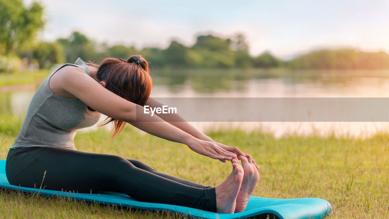 Woman exercising while sitting by lake