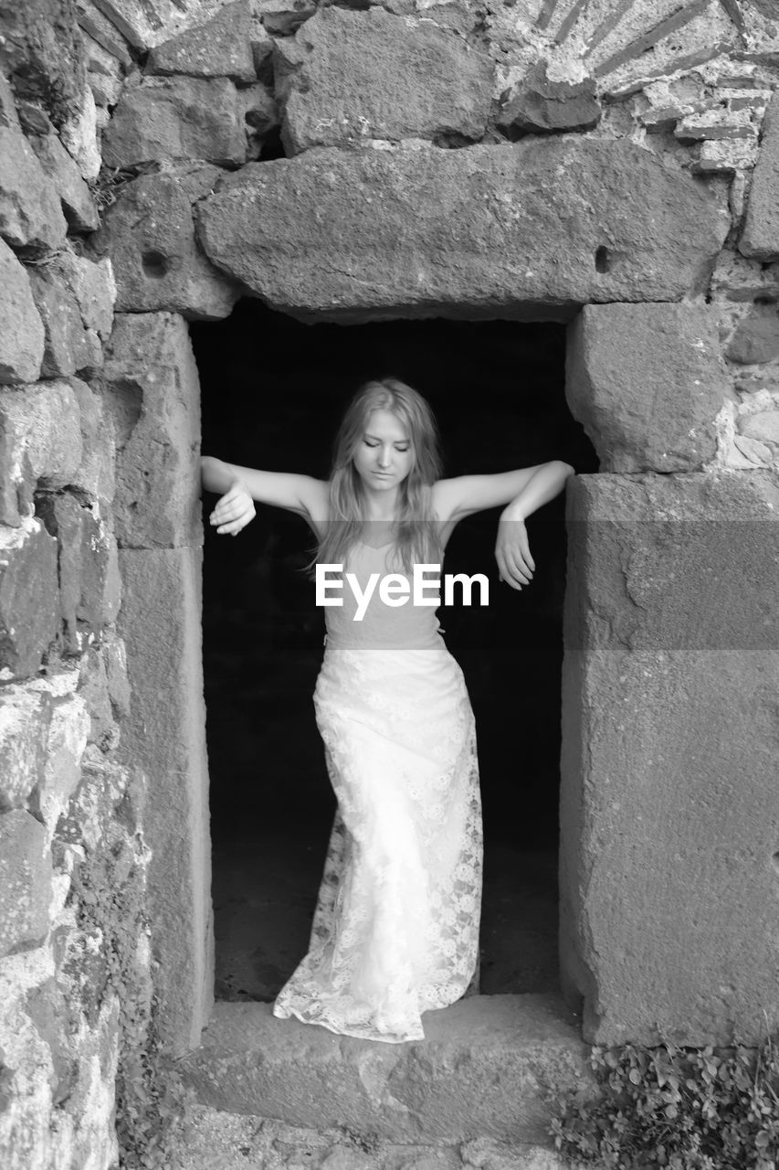 Sad young woman wearing white dress standing on doorway