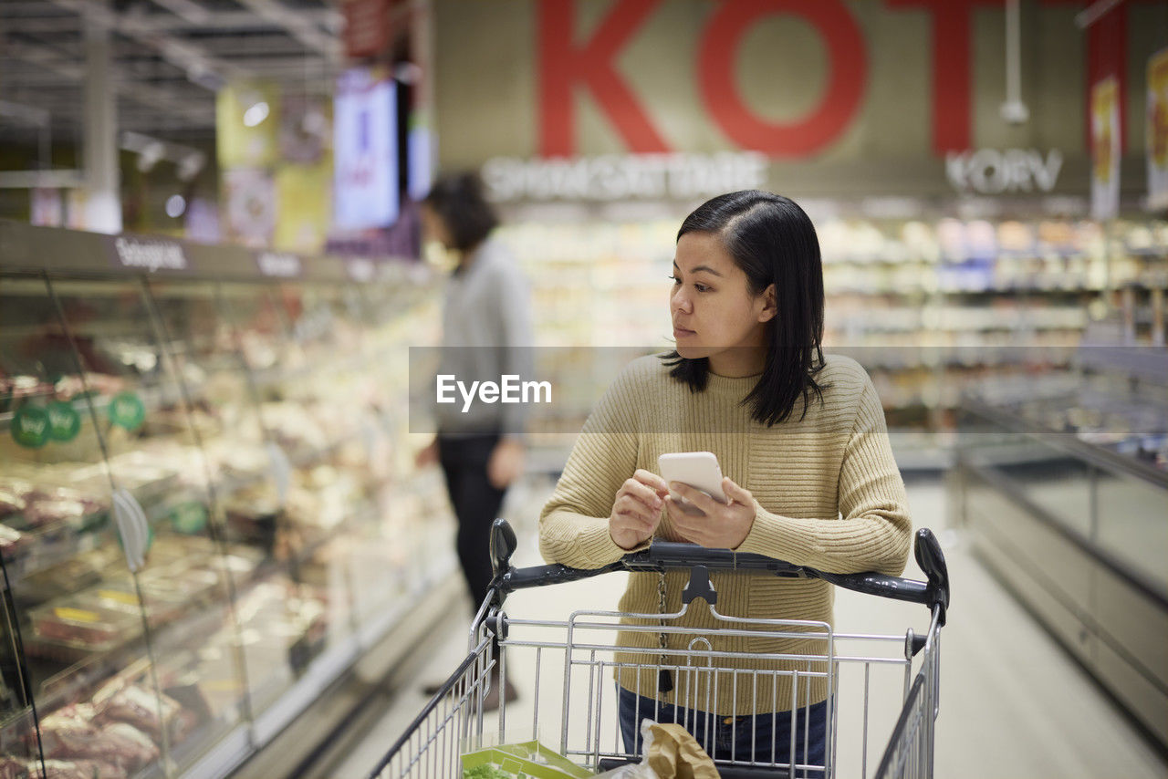 Woman doing shopping in supermarket and holding cell phone