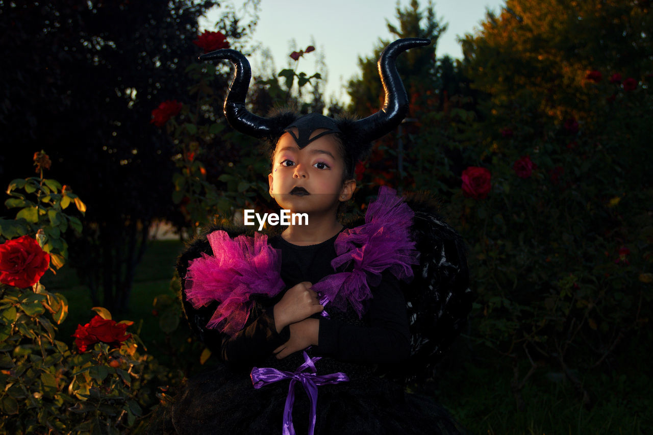 Portrait of young woman with maleficient costume standing against plants