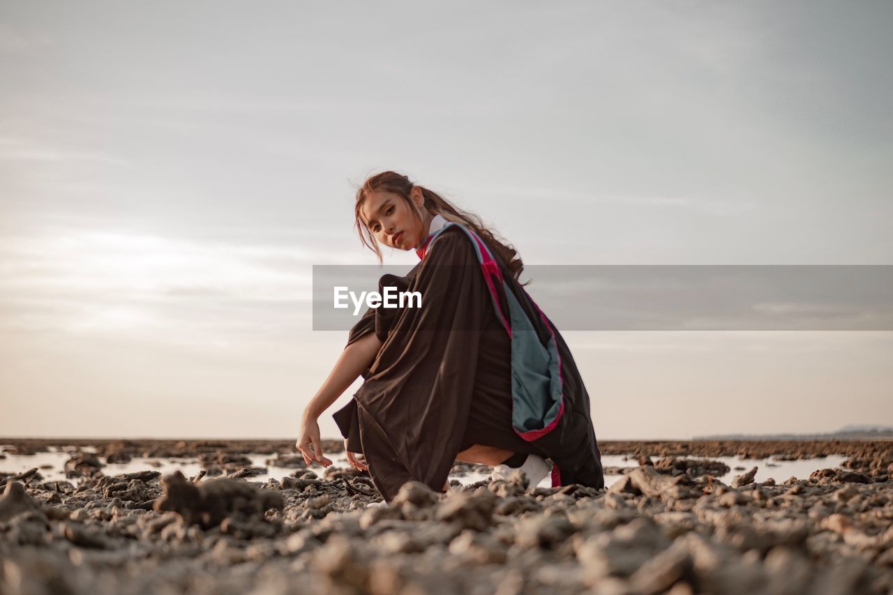 WOMAN ON ROCK BY SEA AGAINST SKY