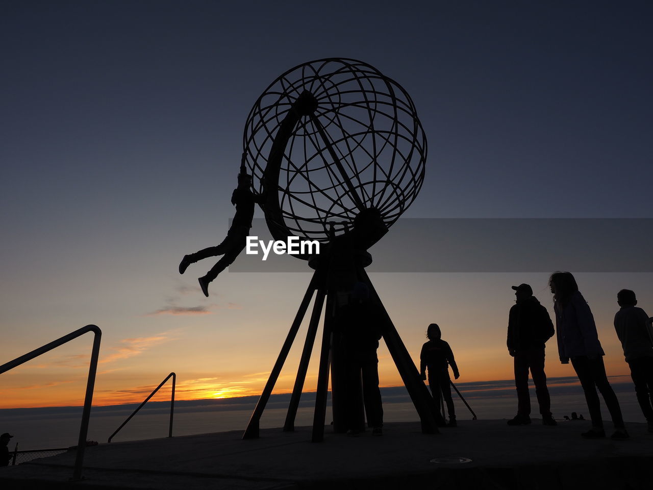 Silhouette people by metallic globe structure against clear sky during sunset