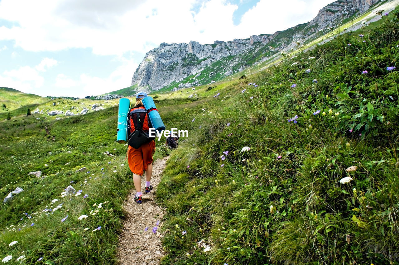 Young woman hiker from behind with backpack hiking on mountain trail in green caucasus mountains