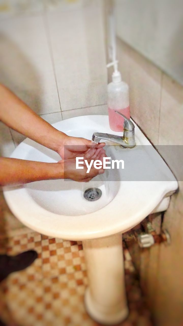 Cropped hands of person washing hands in sink