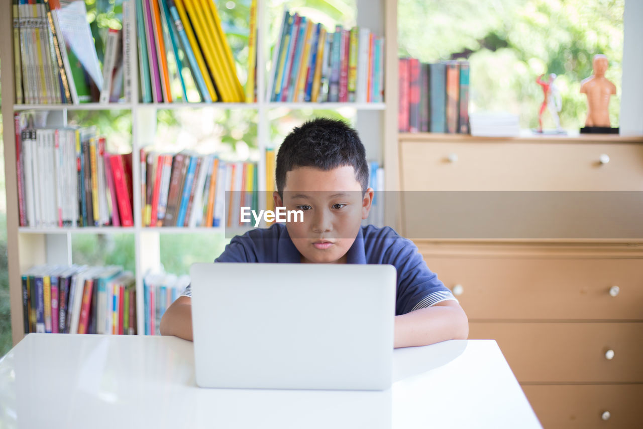 Boy using laptop while sitting at table in library