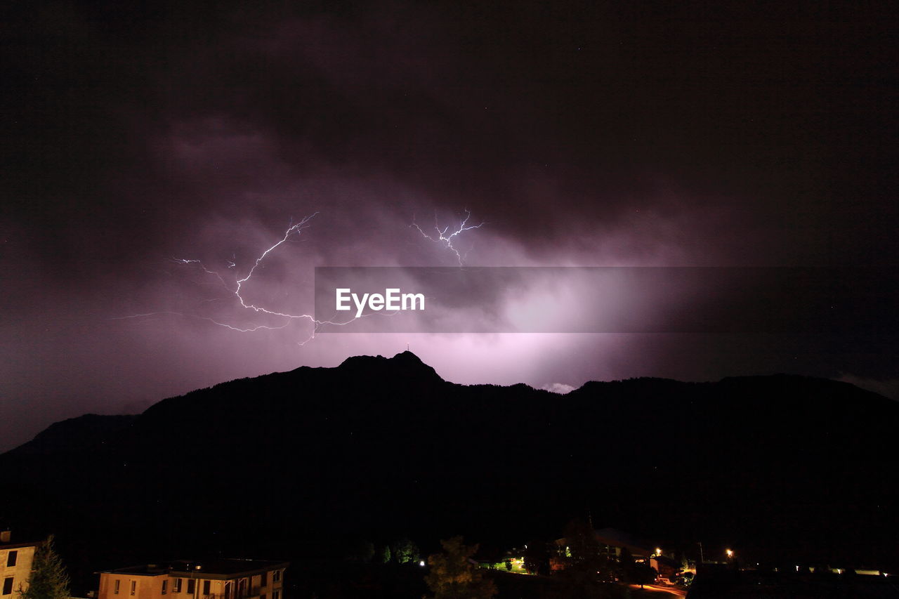 Lightning over silhouette mountains against sky at night