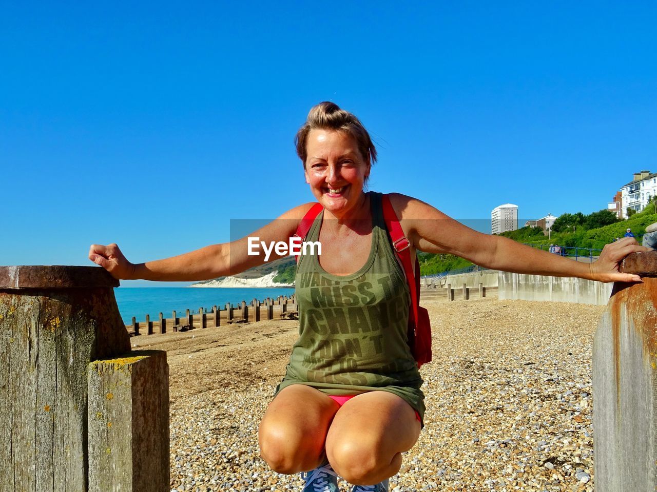 Portrait of smiling woman crouching at beach against clear sky