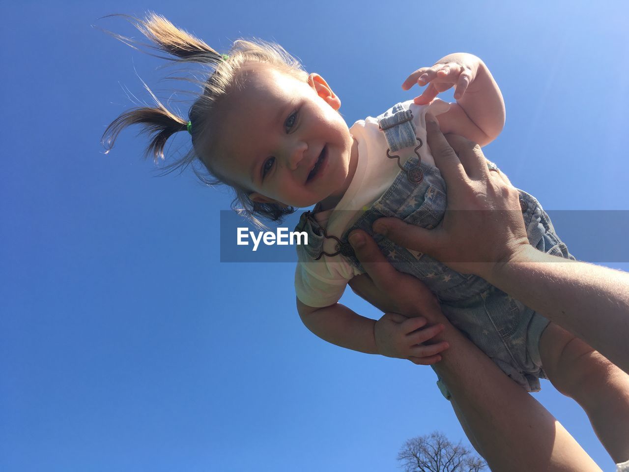 Cropped hands of father picking up cute daughter against clear blue sky