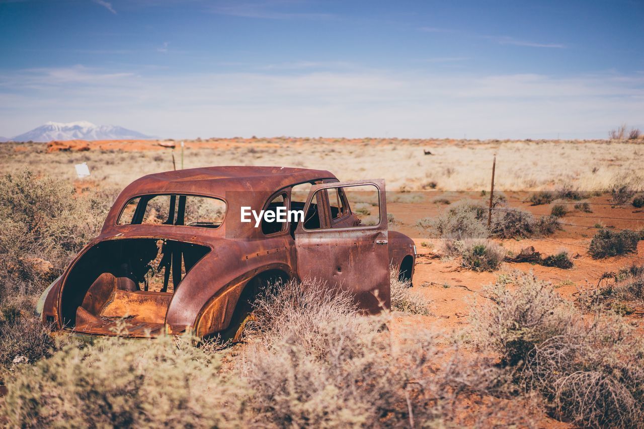 Abandoned car on land against sky