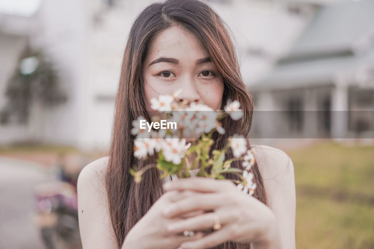 Portrait of woman holding flowers while standing against building