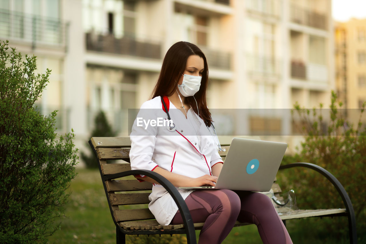 young woman using laptop while sitting on bench