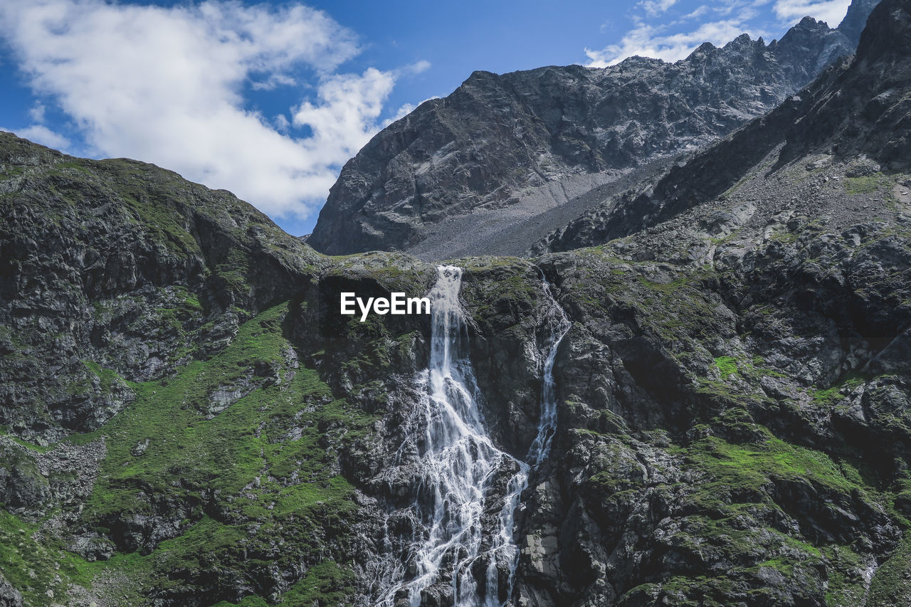 LOW ANGLE VIEW OF WATERFALL AGAINST MOUNTAIN