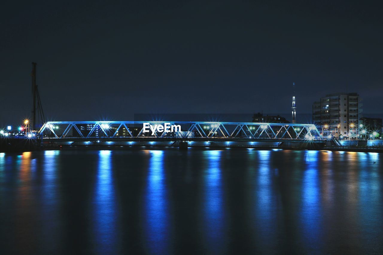 Illuminated bridge over river against sky at night