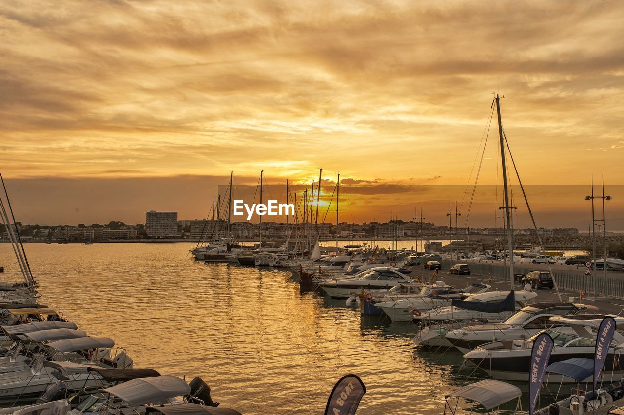 SAILBOATS MOORED IN HARBOR AT SUNSET