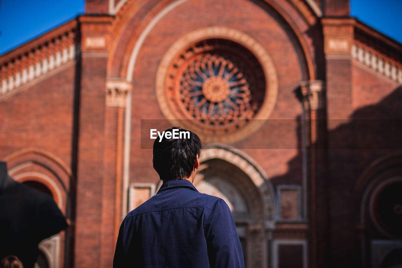 REAR VIEW OF MAN STANDING OUTSIDE TEMPLE