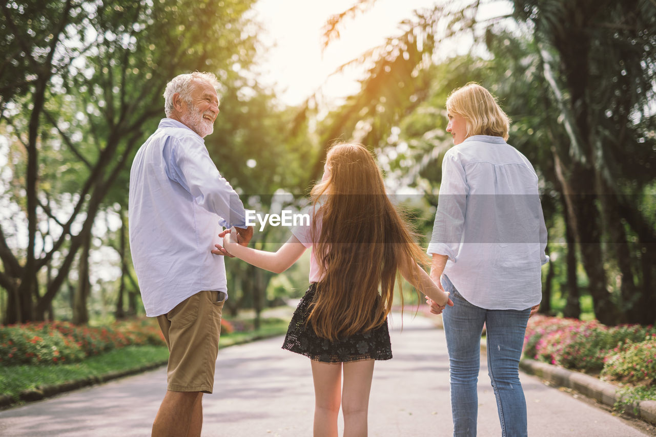 Rear view of girl with grandparents standing on road