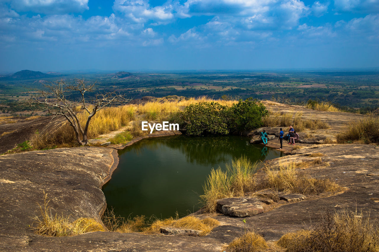 People at pond on mountain against sky