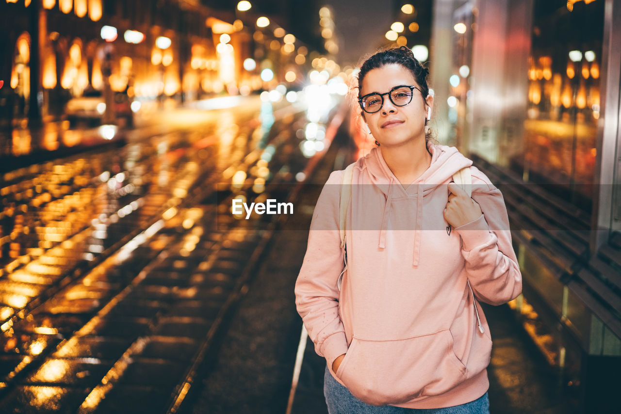 portrait of young woman wearing sunglasses while standing in city at night