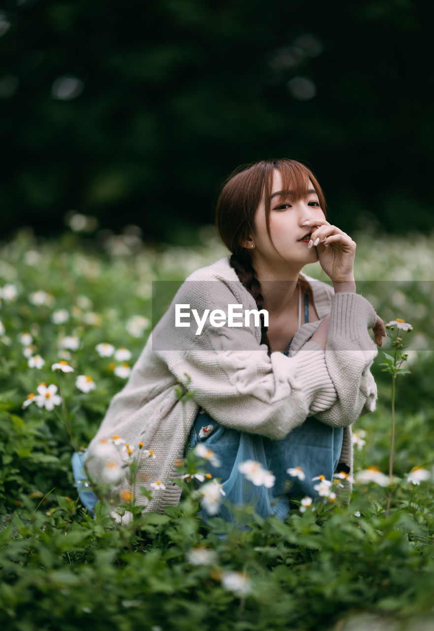 young woman looking away while standing against plants