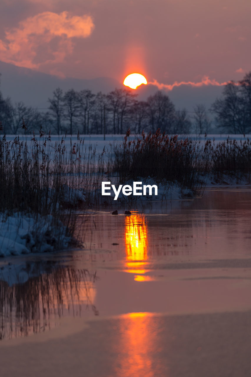 SCENIC VIEW OF FROZEN LAKE AGAINST ORANGE SKY DURING SUNSET