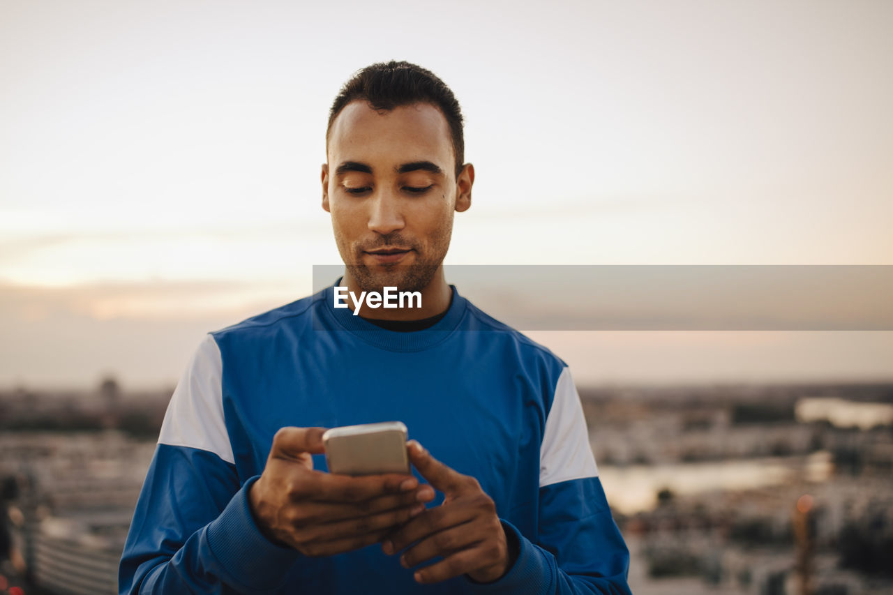 Sportsman using smart phone against sky during sunset