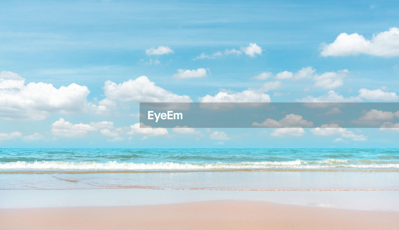 Brown sand beach on blue sea water and white wave under white clouds and pastel blue sky background