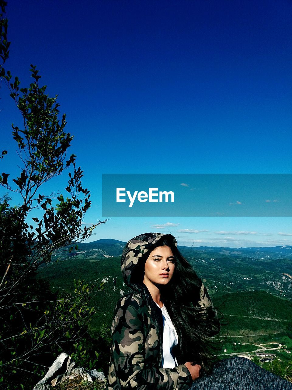 Portrait of young woman wearing camouflage clothing against blue sky