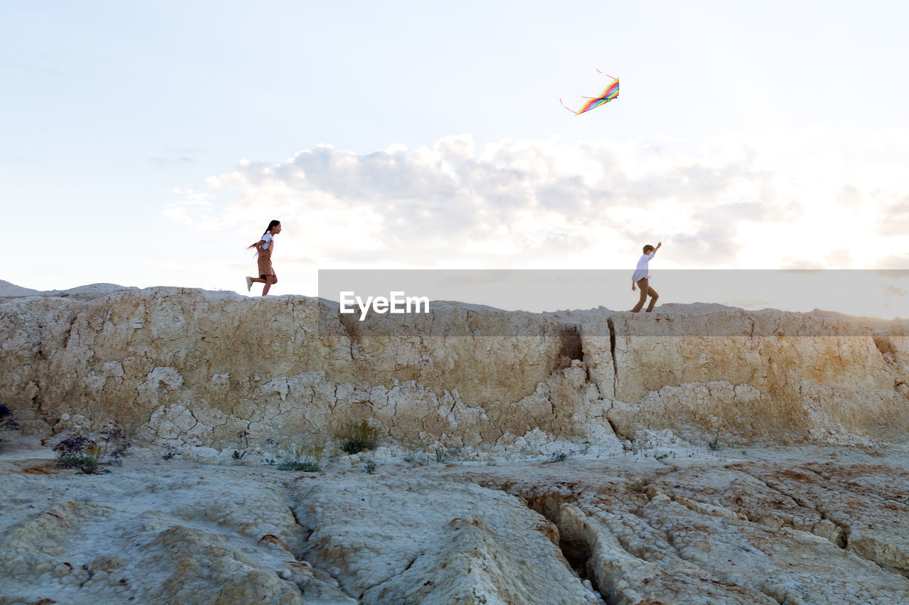 A boy and a girl running with kite on the mountainside.