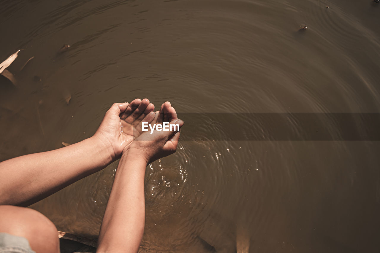 Cropped image of hands holding water over lake