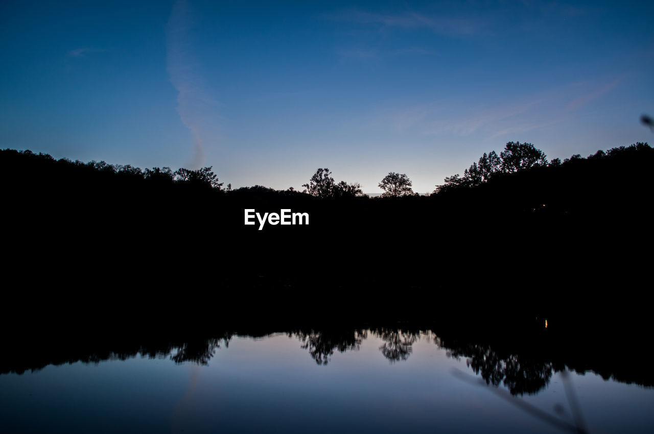 REFLECTION OF SILHOUETTE TREES IN LAKE AGAINST SKY