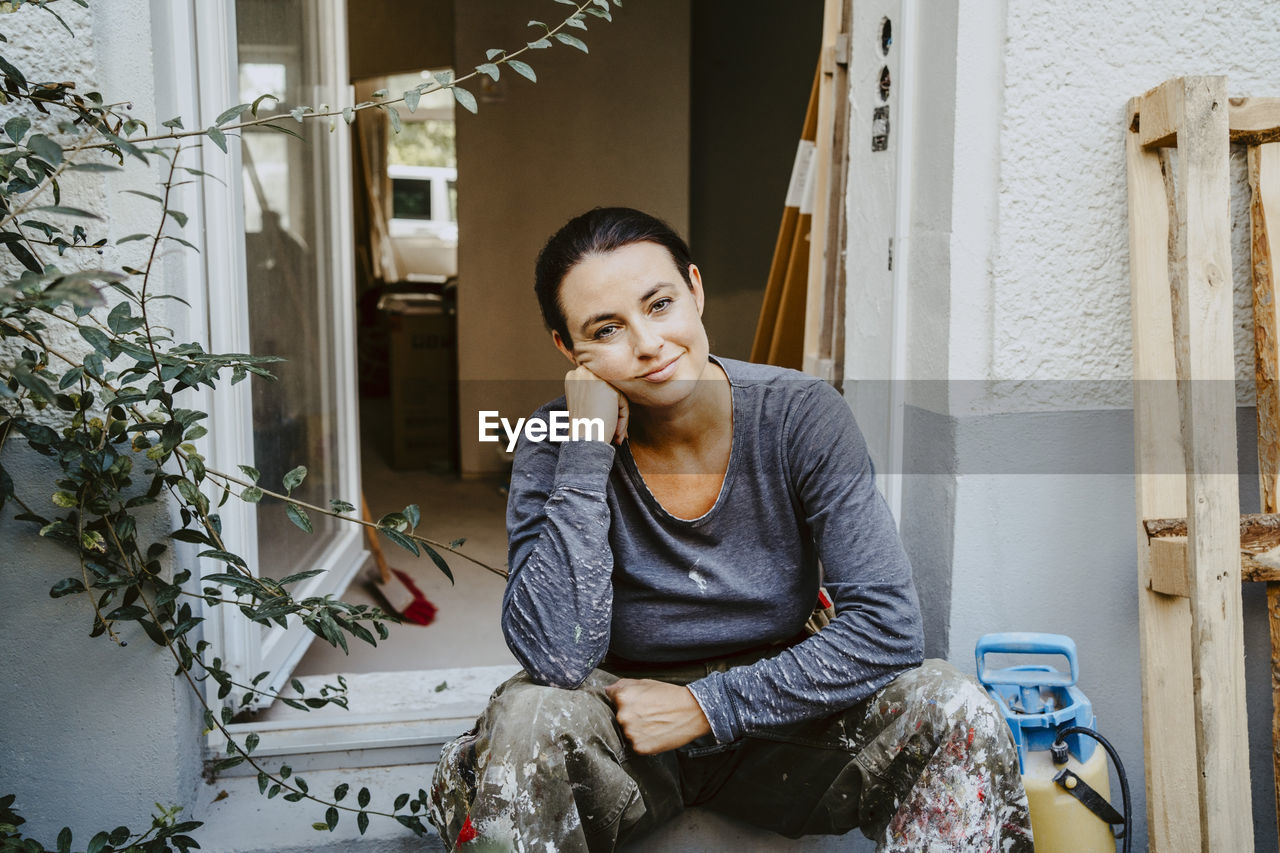 Portrait of smiling female carpenter sitting at entrance of house