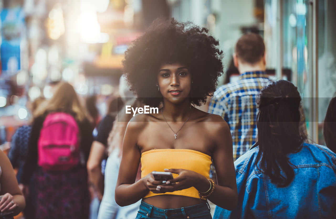 Portrait of confident young woman holding smart phone on city street