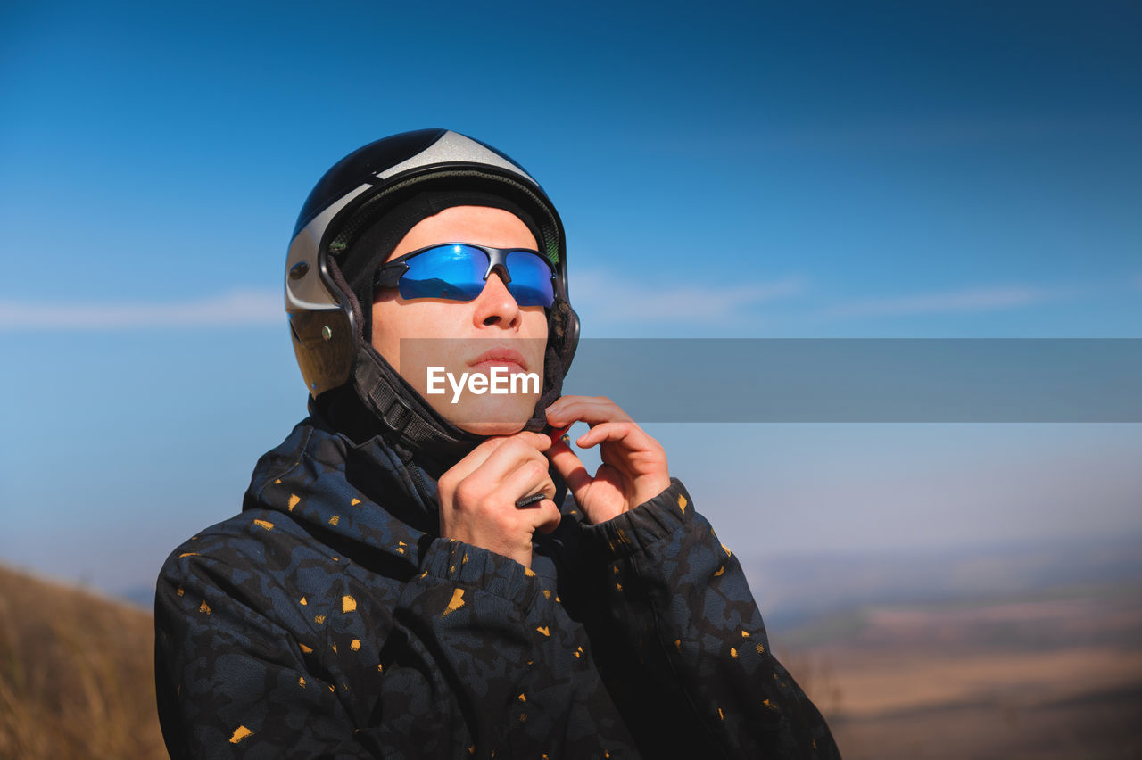 A young male paraglider in sunglasses fastens his helmet on a sunny day. preparing for paragliding