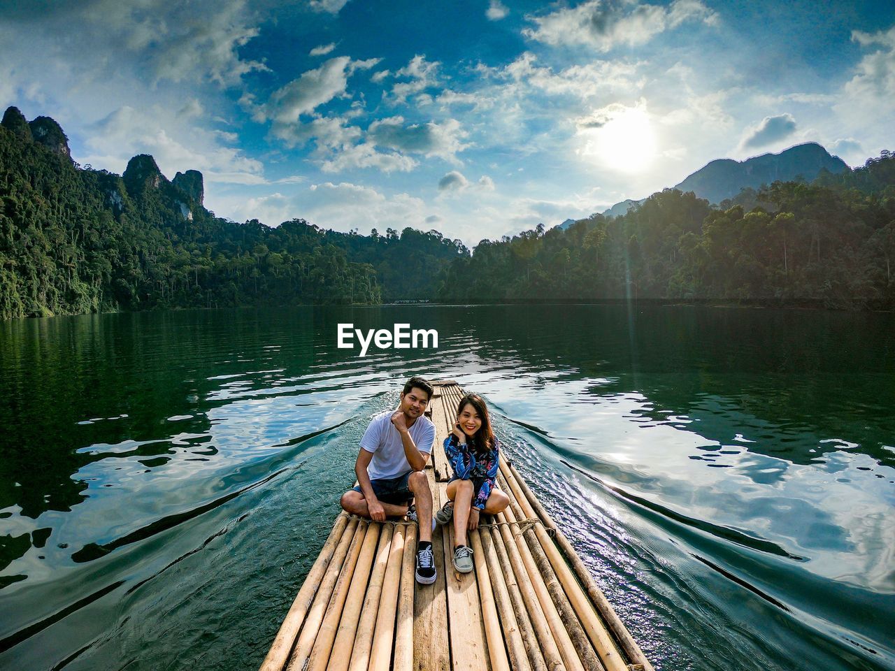 Couple sitting on wooden raft in lake against trees