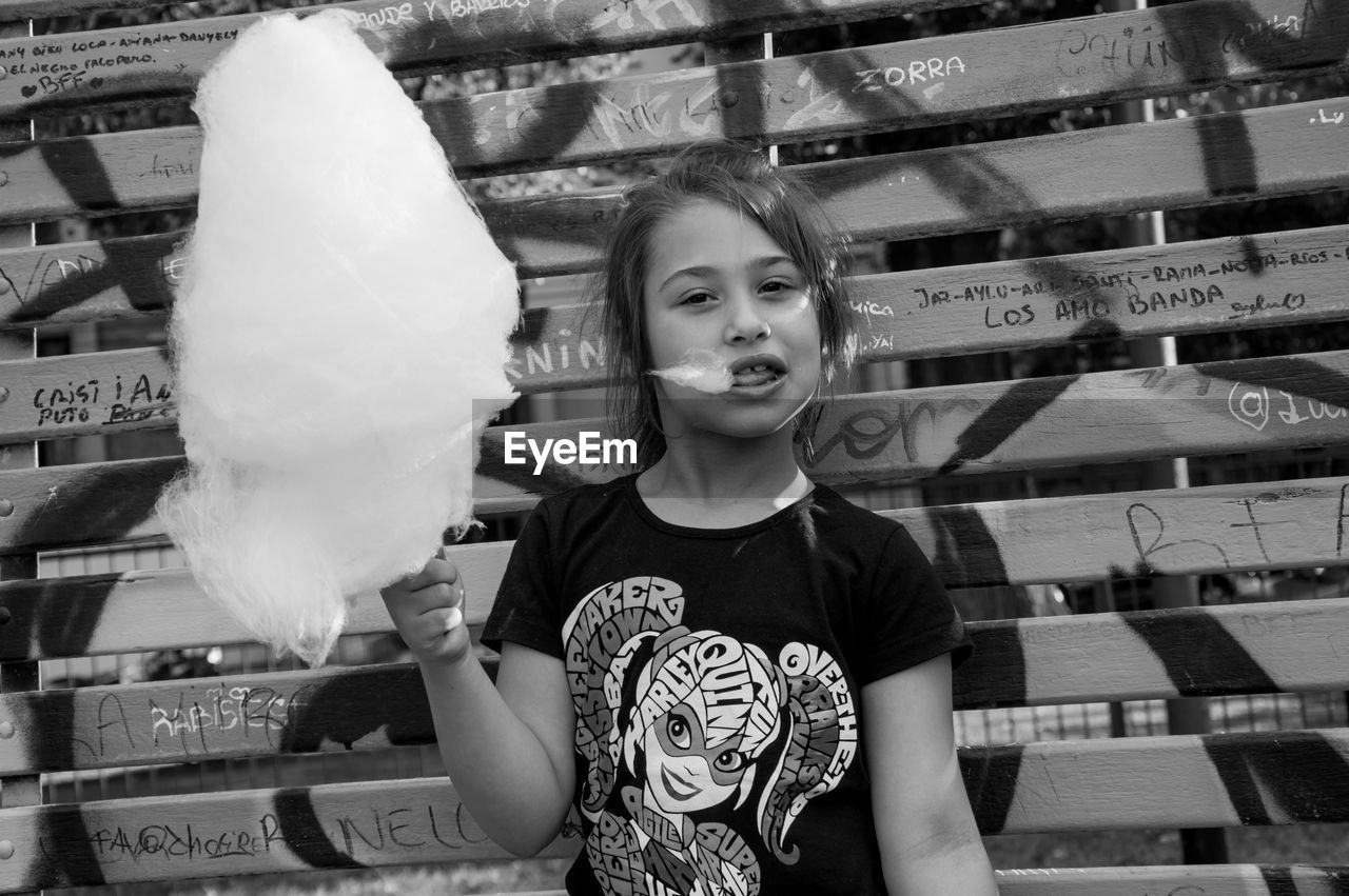 Portrait of girl with cotton candy standing against wall