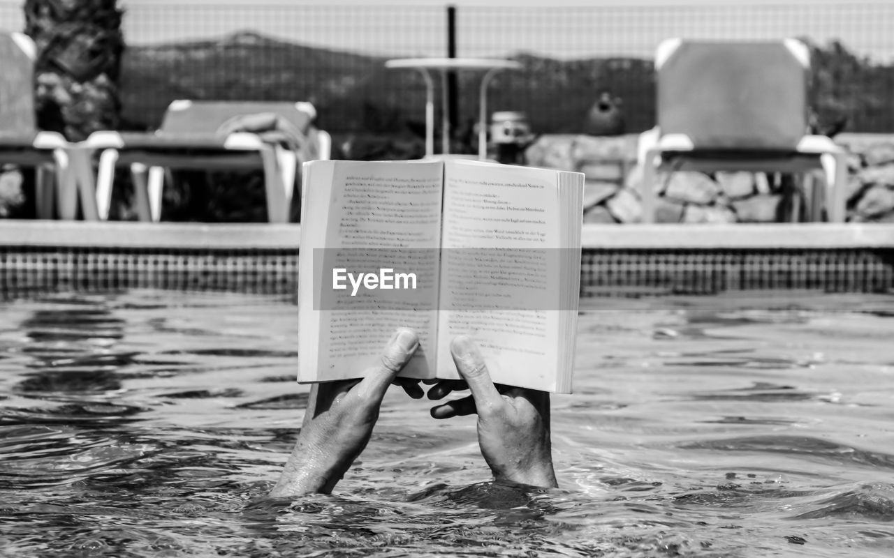 Hands holding novel in swimming pool