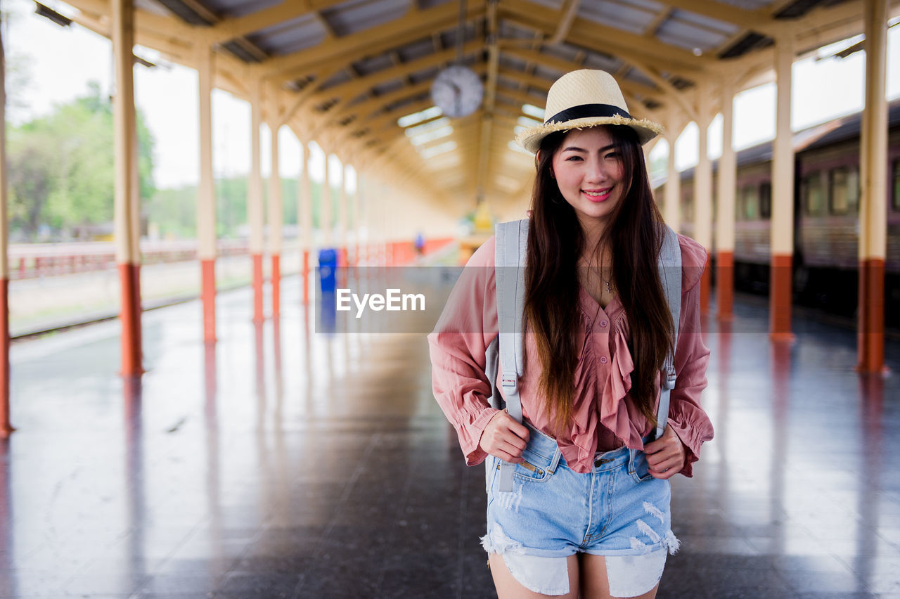 Portrait of smiling woman in hat standing at railroad station platform