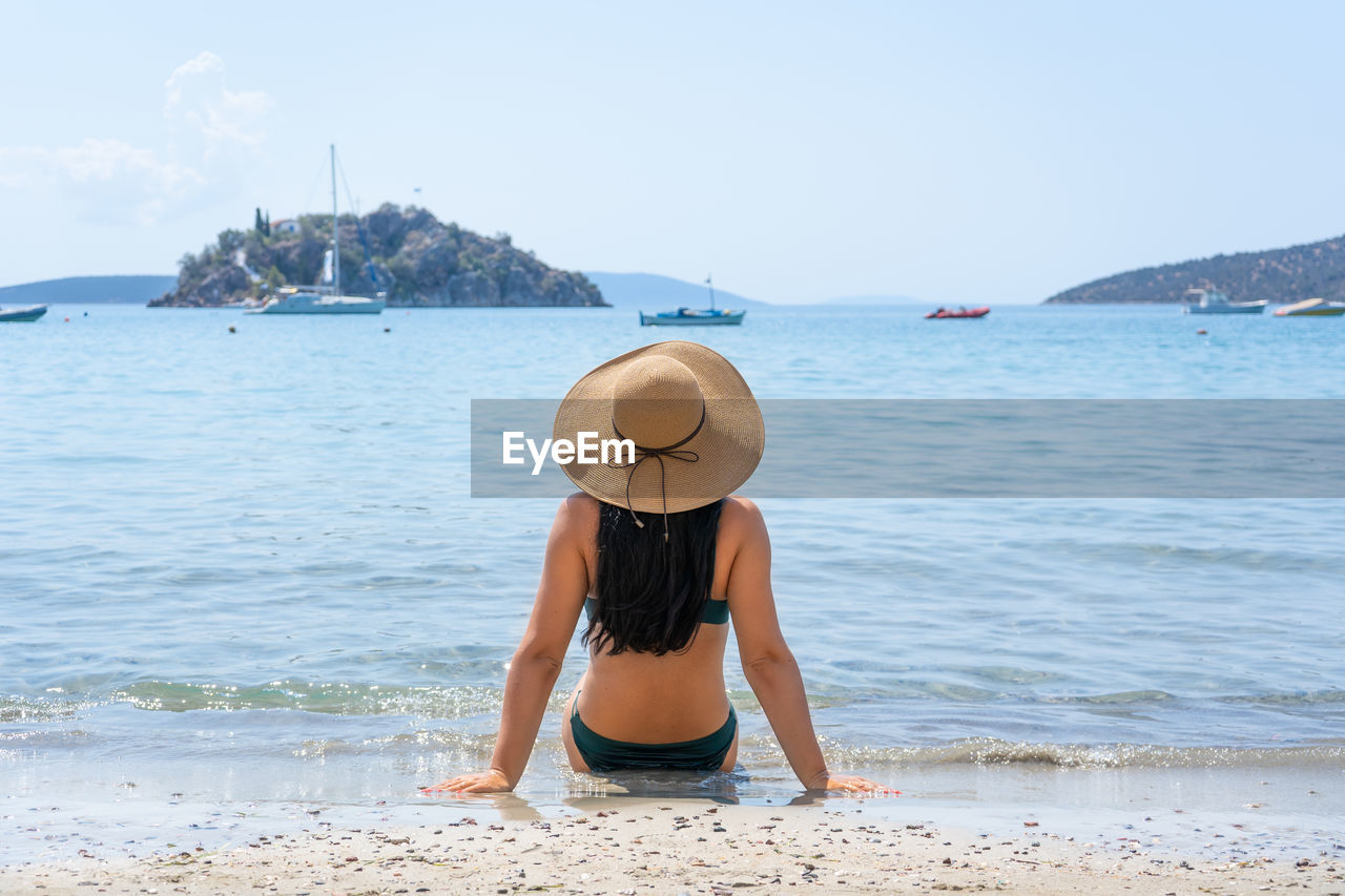 Young girl from the back in a straw hat on the background of the sea bay